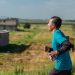 A man jogs in rural area wearing sportswear, emphasizing fitness and determination.