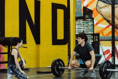 Two young adults in a gym participating in a weightlifting session, sharing a positive moment.